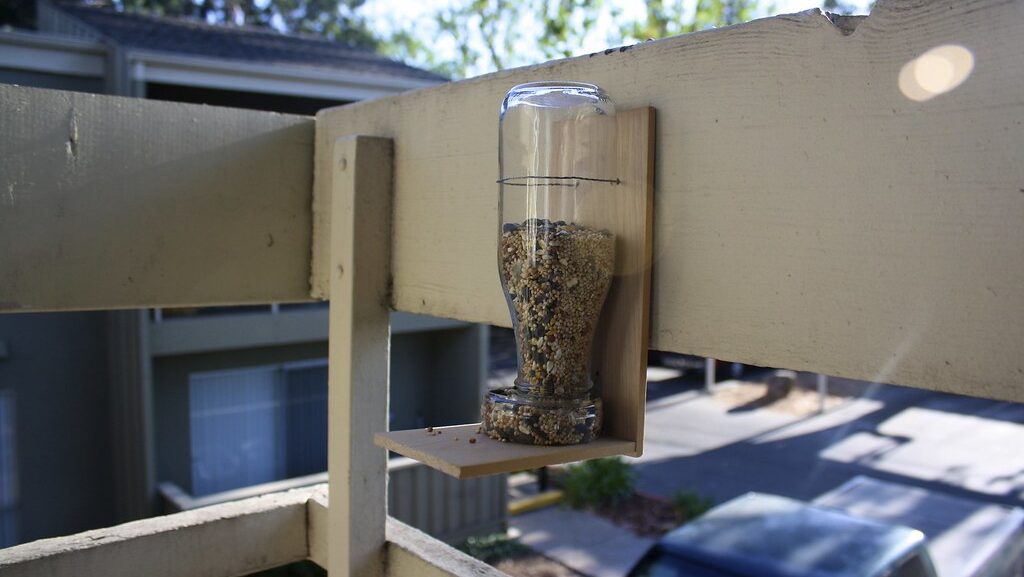 Homemade bird feeder mounted on a wooden deck railing