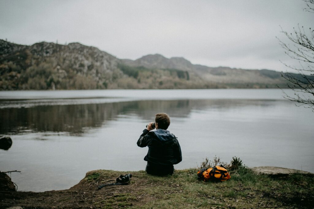 A person sits by a lake, drinking water.