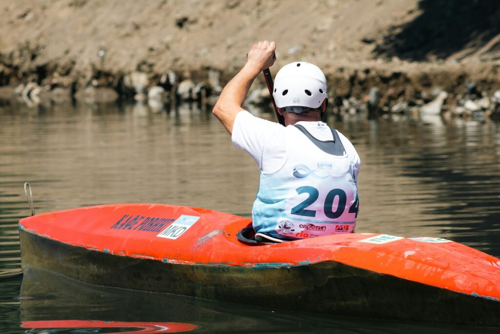 A person in a white helmet paddles a red canoe on a river.
