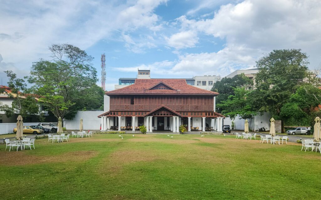 A building with a red tile roof and white pillars sits on a green lawn.