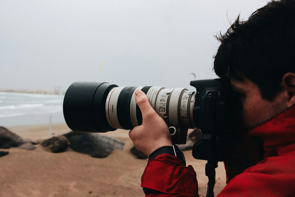 A person in a red jacket holds a camera with a large lens.