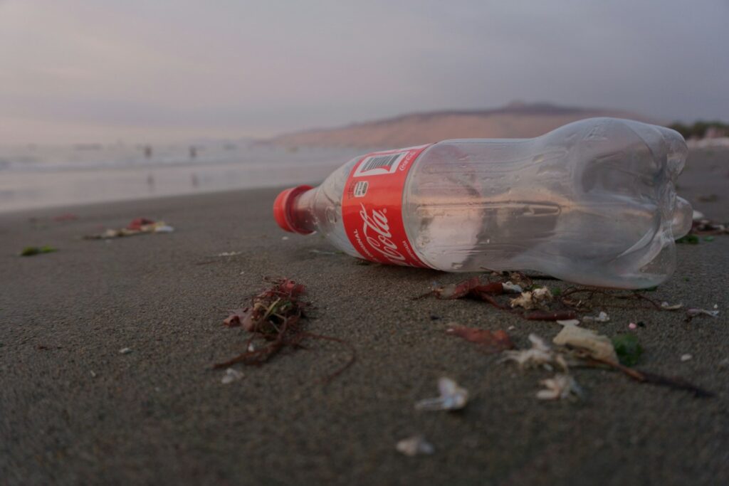 A Coca-Cola bottle lies on a sandy beach.