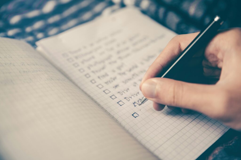 A hand writes on a to-do list in a notebook.