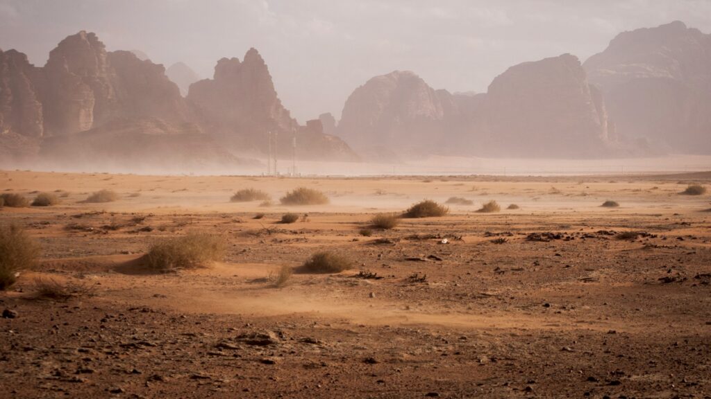 Wide view of a dusty desert valley with arid terrain and rocky hills