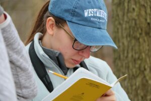 A person with glasses and a blue cap is writing in a notebook.