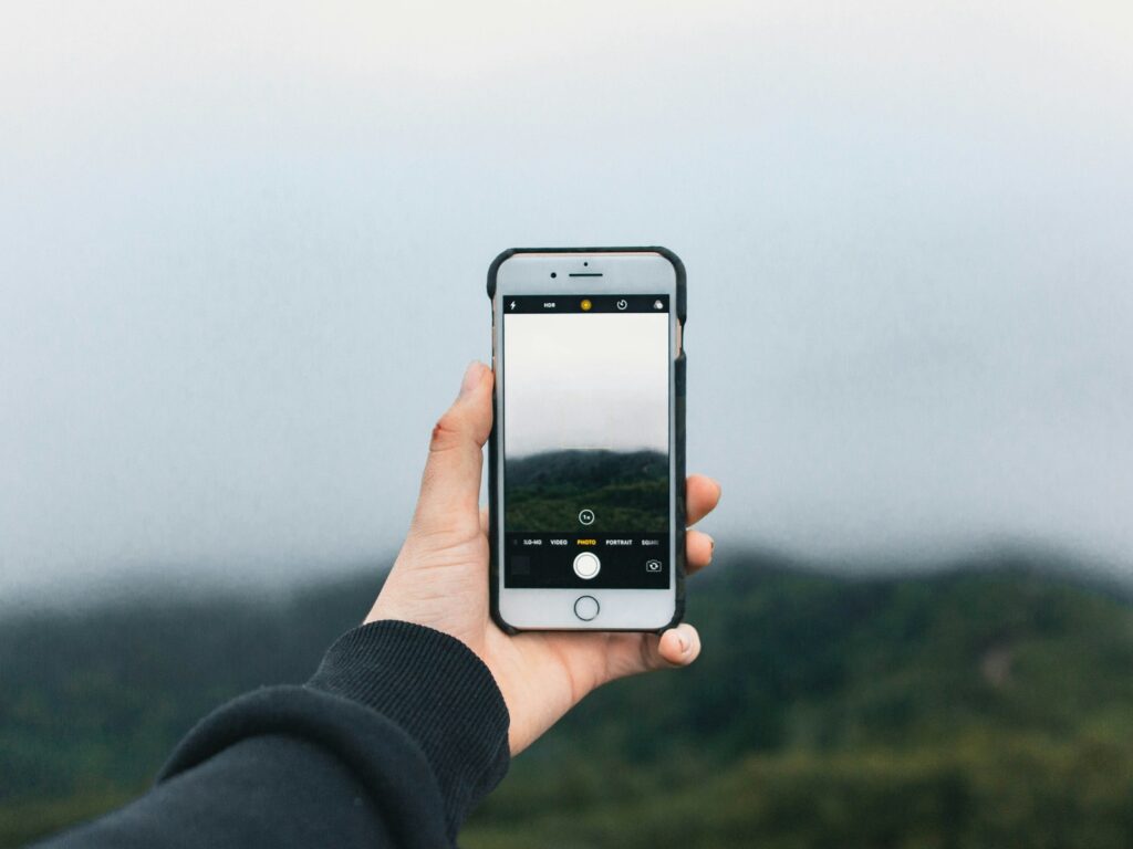 A hand holds a smartphone displaying a landscape photograph on its screen.