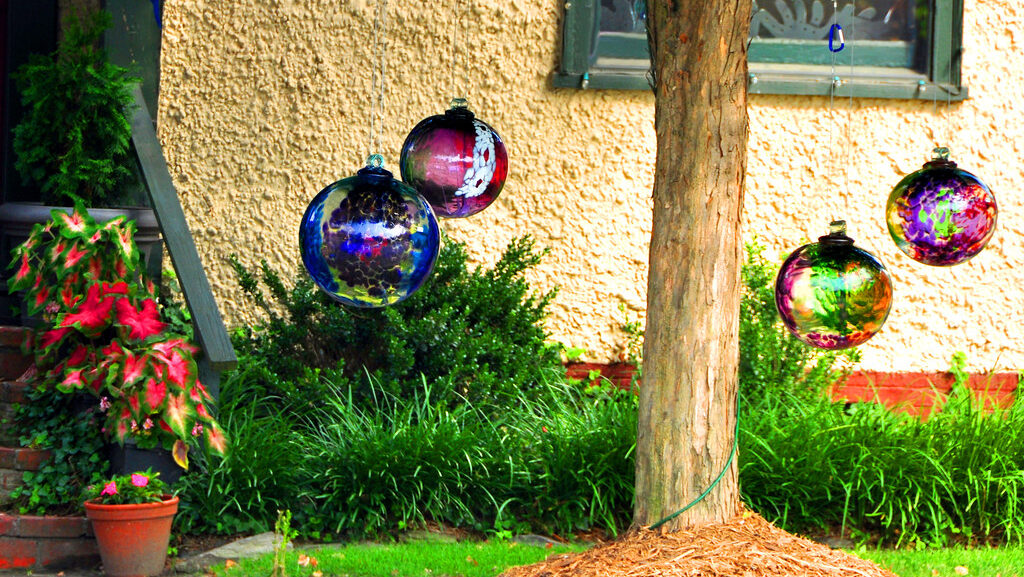 Decorative yard globes hanging from tree branches in a garden