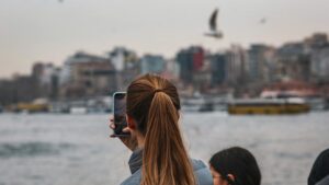 Woman photographing harbor scene with birds flying overhead