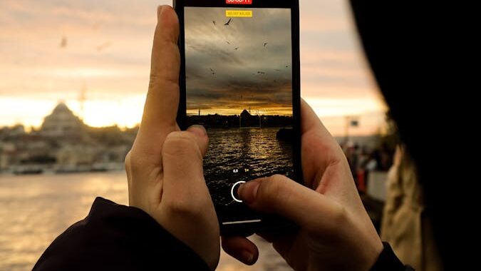 Person capturing stunning seaside sunset with flying birds on smartphone