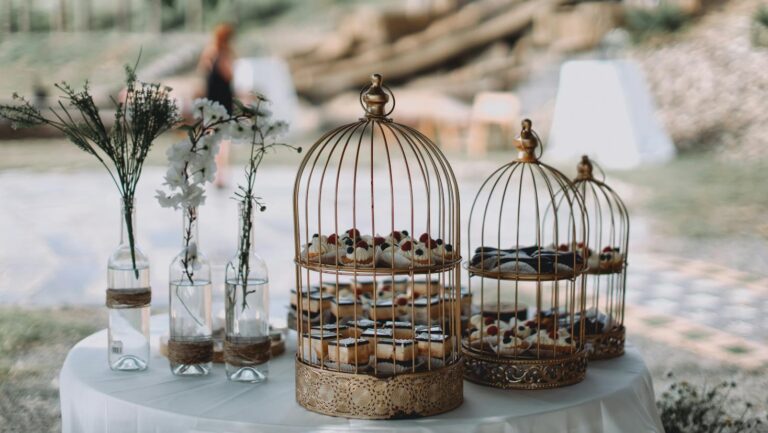 Elegant outdoor garden party table with decorative cakes inside birdcages and fresh floral arrangements