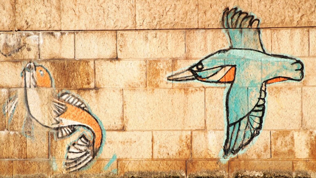 A graffiti art piece on a brick wall depicts a flying bird and a fish.