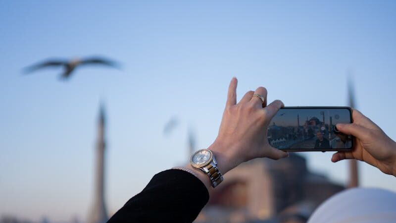 Person photographing architectural spires under clear sky with birds flying above