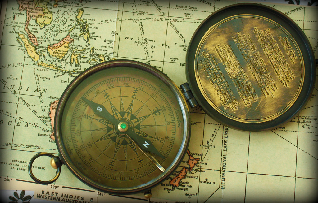 An open brass compass with intricate details rests on a vintage map.