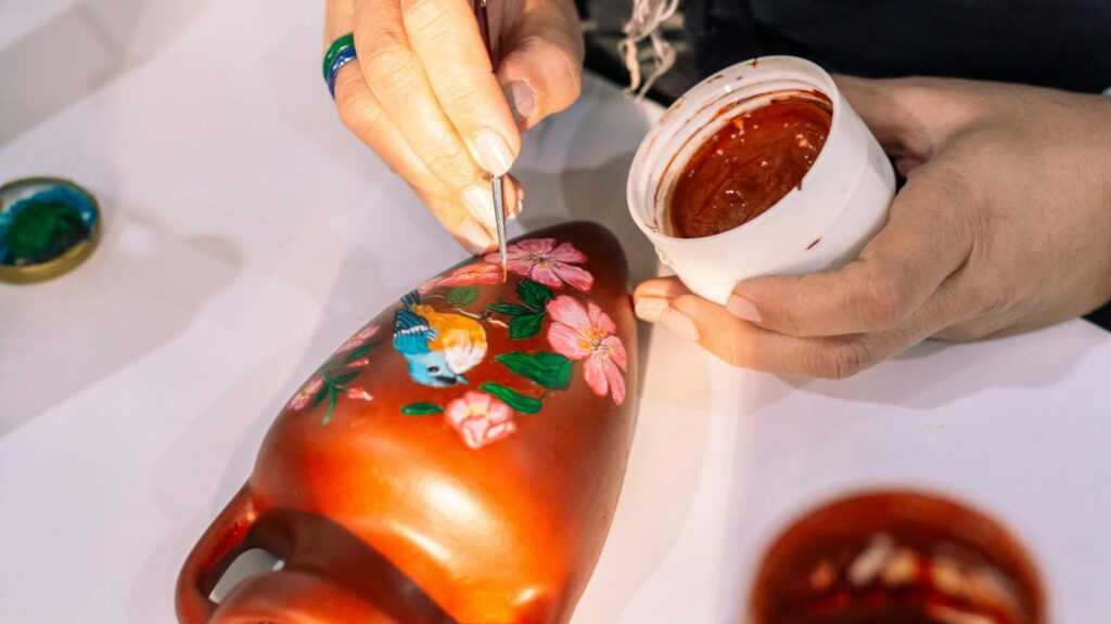 An artist painting a colorful bird on a clay vase
