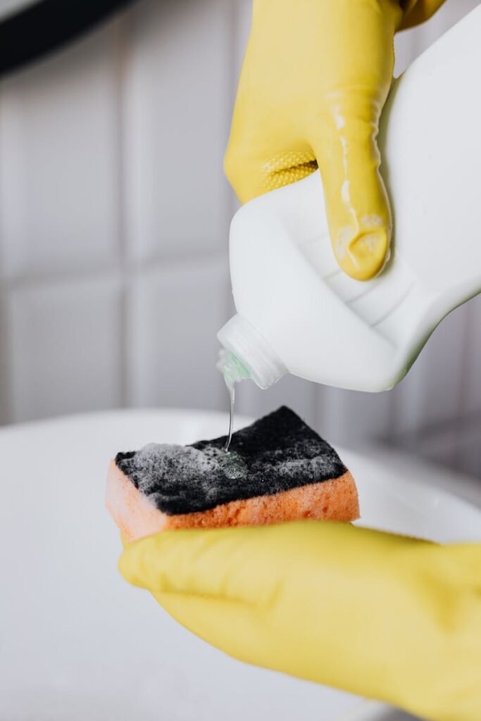 Hand pouring liquid cleaner onto sponge for cleaning