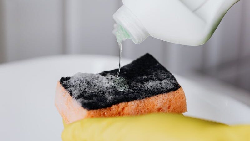 Hand pouring liquid cleaner onto sponge for cleaning