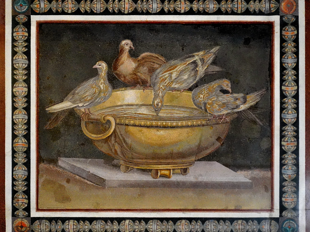 A Roman mosaic shows four doves drinking from a golden bowl, set against a dark background.