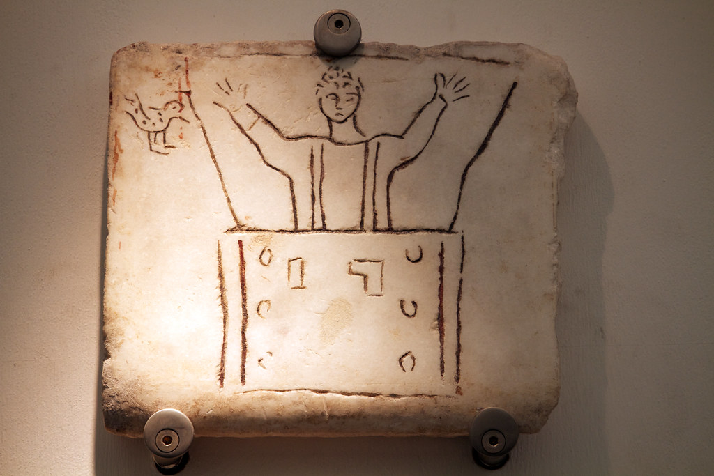 An ancient carving on stone shows a figure with raised arms and a small bird.