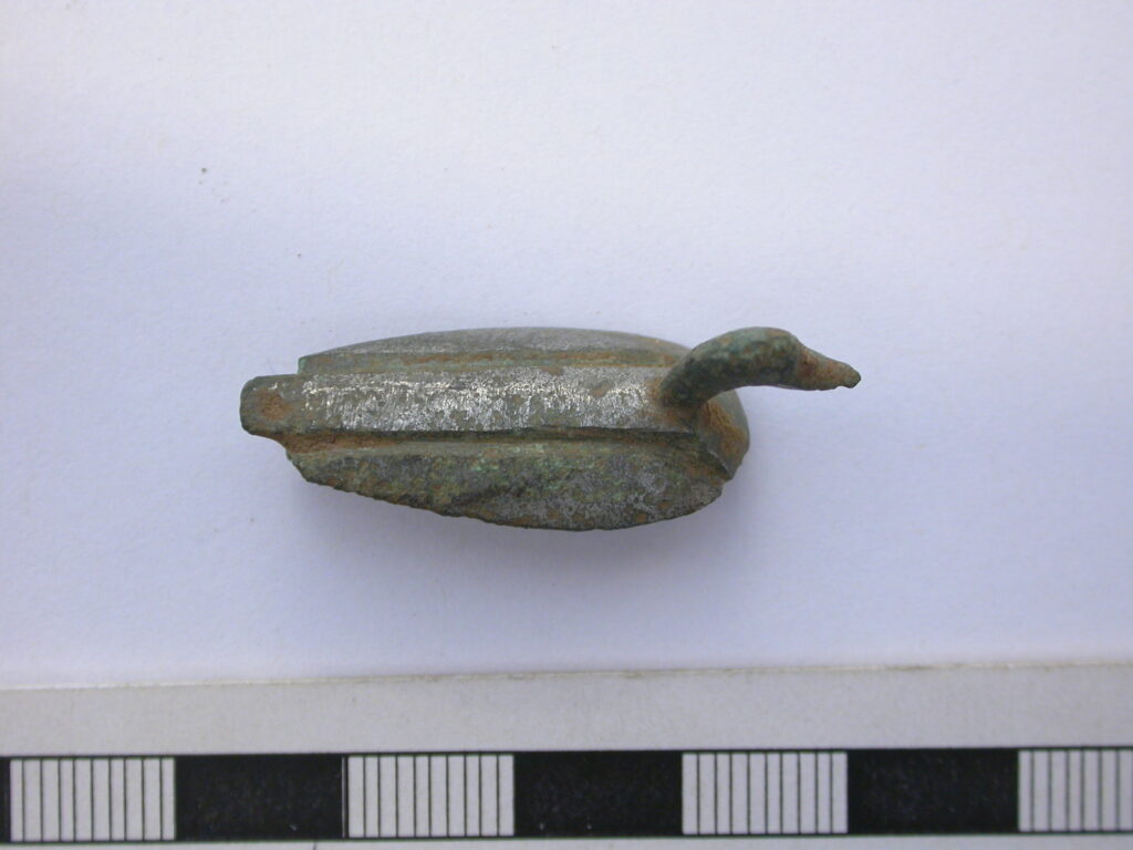 A small, aged metal object resembling a duck, with a textured body and distinct head.