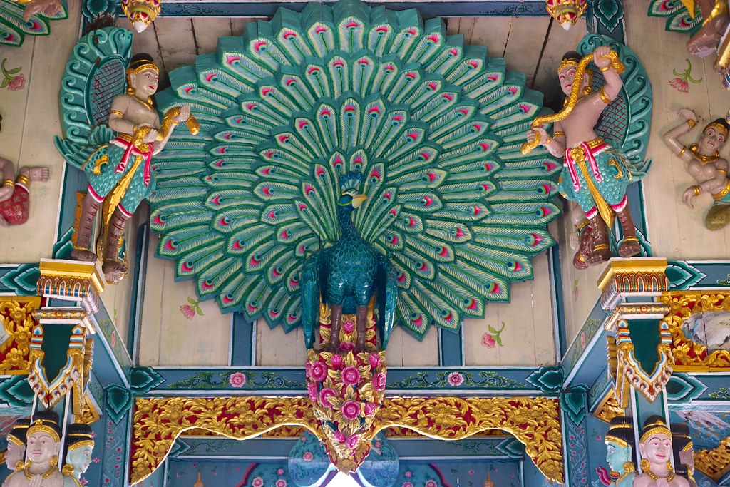 A vibrant, carved peacock with an open tail is part of an ornate temple decoration.