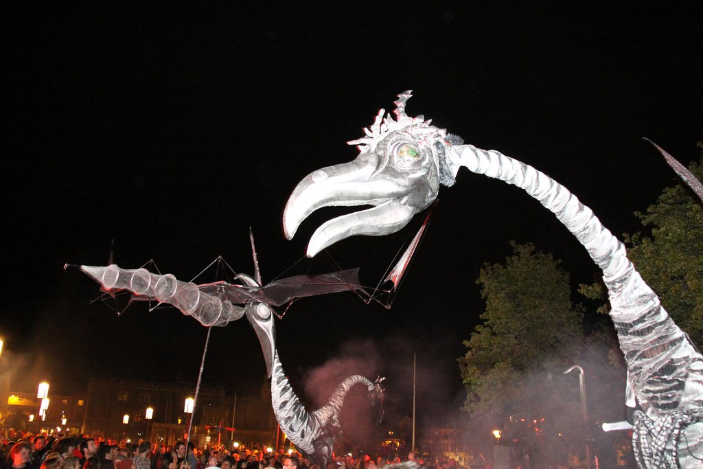 Large bird-like puppets with long necks and open beaks stand under a dark sky.