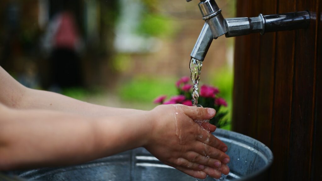 Person washing hands with running water over a bucket
