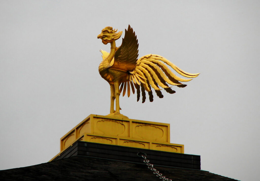 A gleaming golden phoenix statue with detailed wings stands atop a dark-roofed structure.