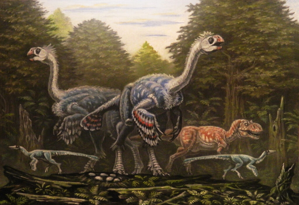 An illustration depicts a Gigantoraptor with feathered arms and two smaller dinosaurs.