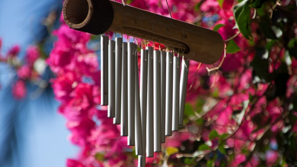 Metal wind chime hanging from a tree branch in a peaceful backyard