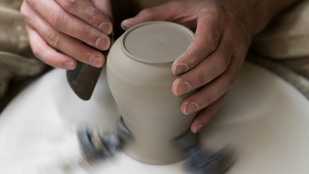 Hands shaping a clay pot on a spinning pottery wheel