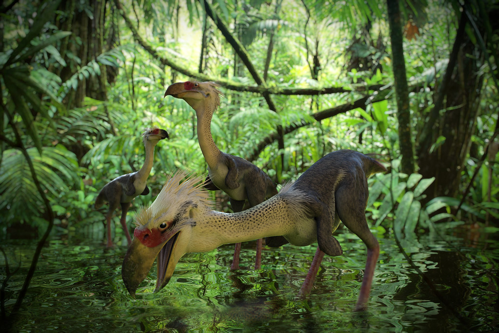 A trio of Kelenken birds, with long necks and beaks, stand in shallow water amidst dense jungle foliage.