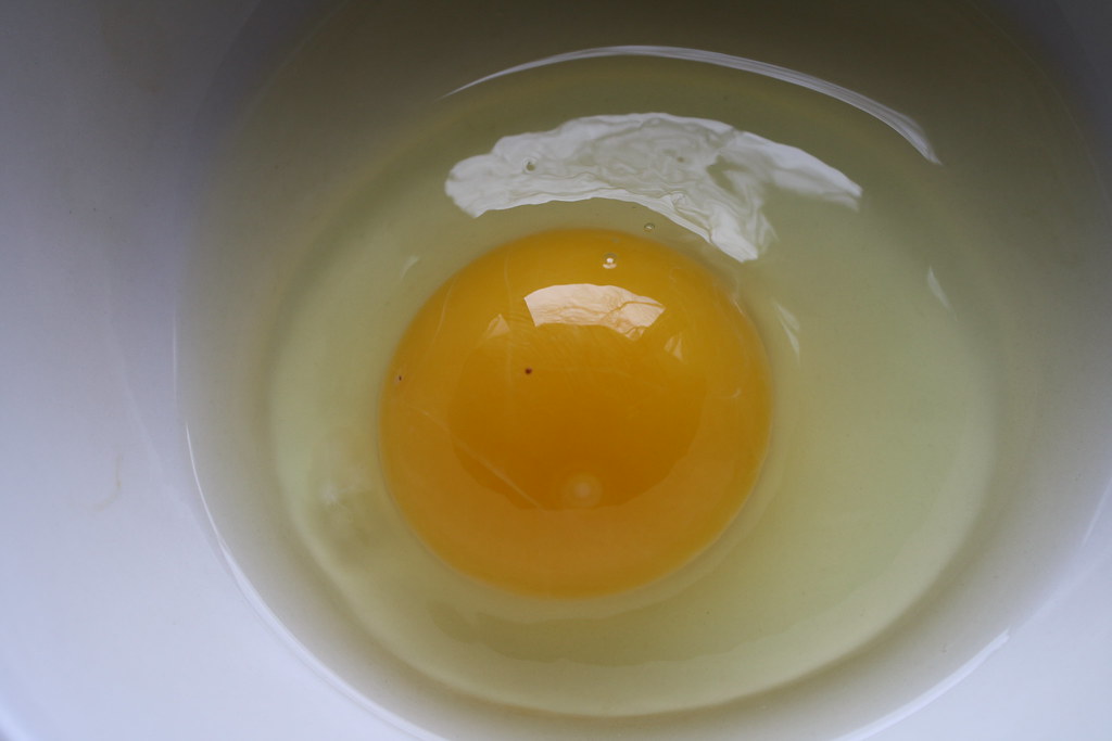 A bright yellow egg yolk rests within the clear egg white in a white bowl.