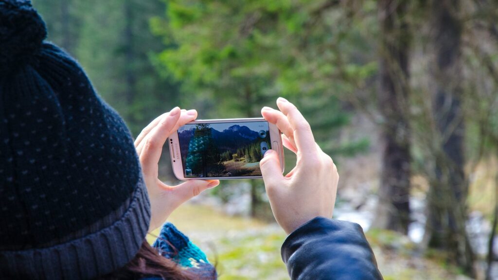 Person holding smartphone taking photo in a forest