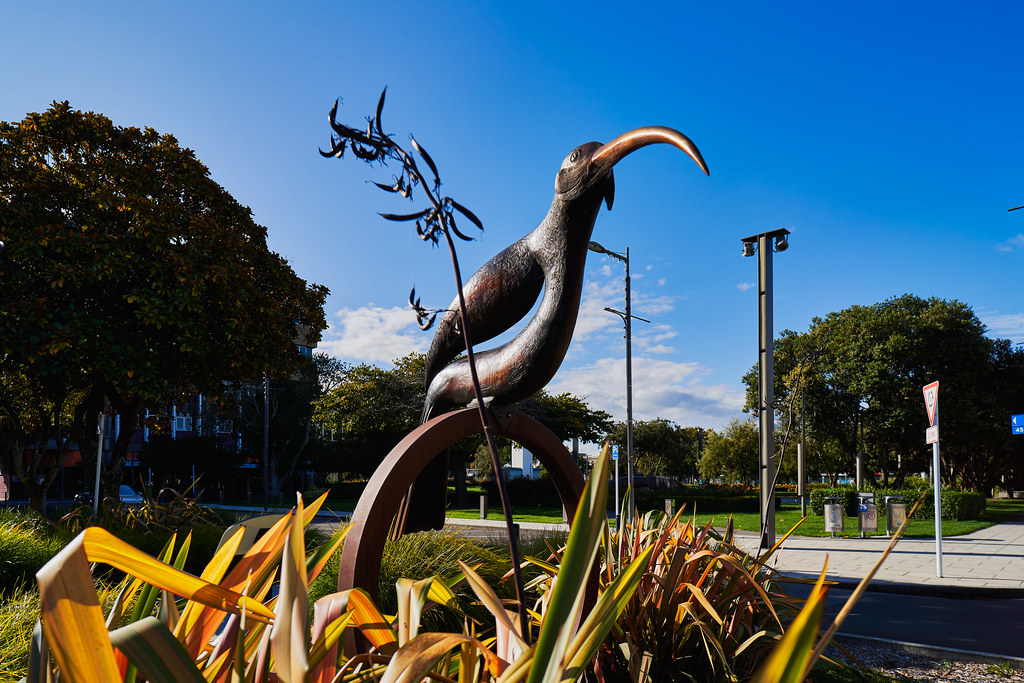 A dark bronze Huia bird sculpture with a curved beak, adorned with metallic leaves.