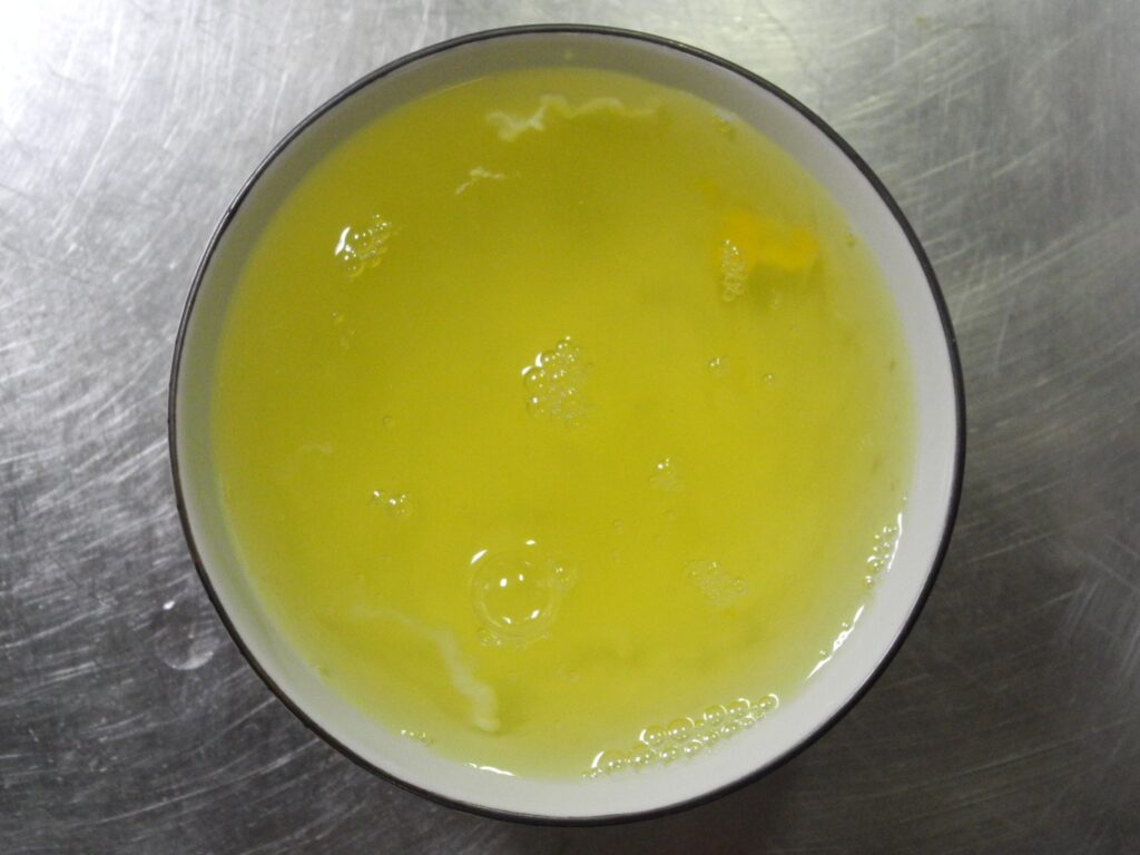 A bowl is filled with clear, pale yellow egg whites with a few bubbles on the surface.