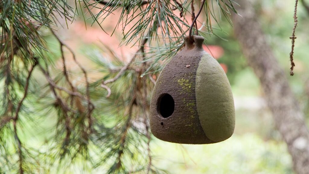 Handcrafted brown and yellow clay pot birdhouse hanging in a garden