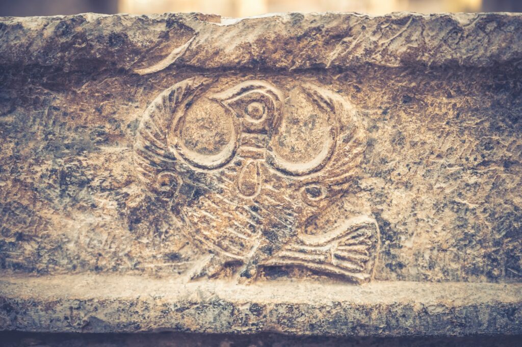 A rustic stone carving shows a stylized owl with large, round eyes.