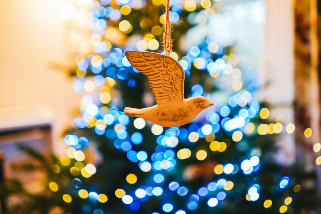 A decorative wooden dove ornament hangs in front of blurred Christmas lights.