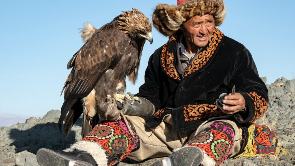 Kazakh eagle hunter sitting with Golden Eagle perched on gloved arm