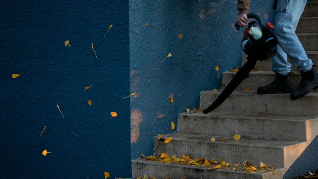 Man standing on outdoor stairs using leaf blower to clear leaves