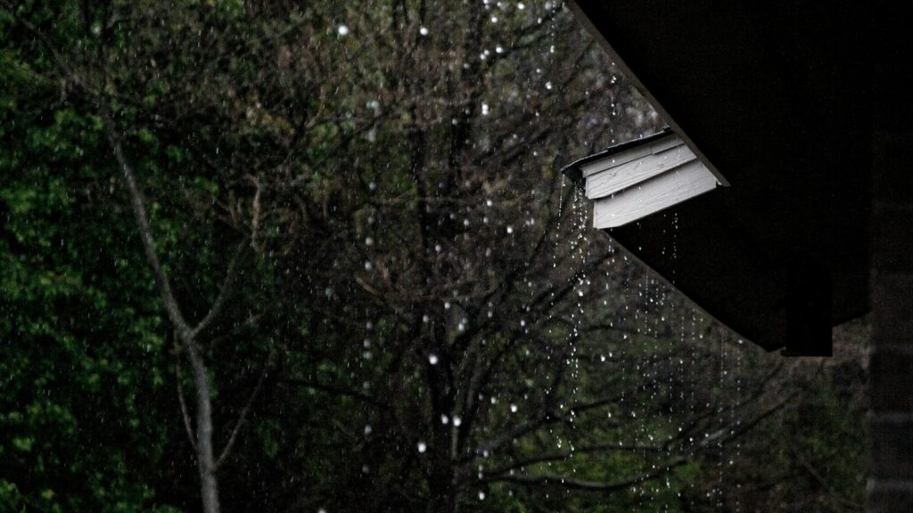 Raindrops streaming down the roof of a home during a rainy day