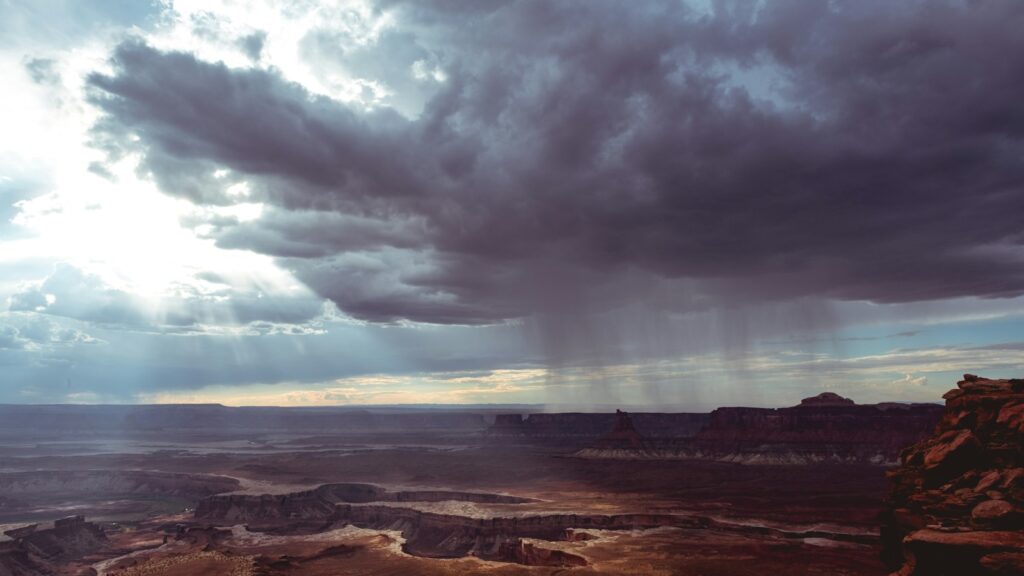 Dark storm cloud releasing rain over a section of arid desert landscape