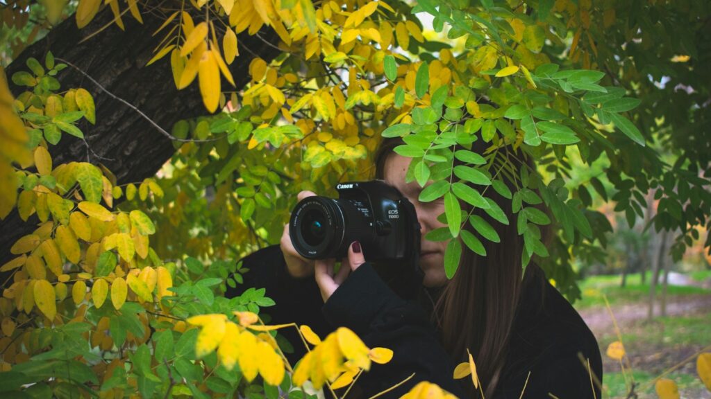 Person holding camera partially covered by leaves